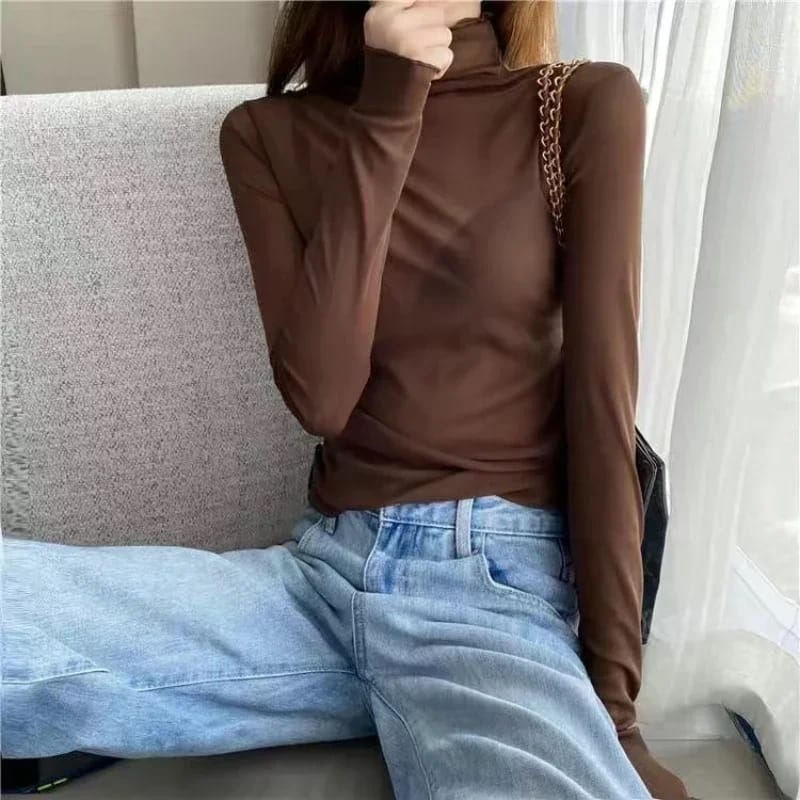 Person wearing a brown turtleneck and blue jeans sitting on a couch.
